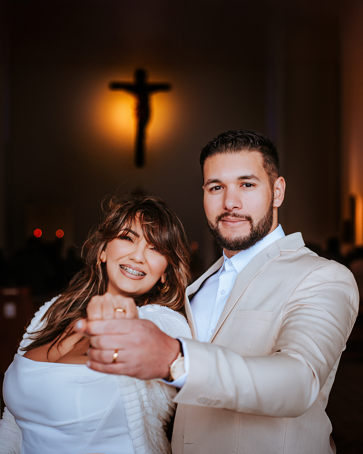 Retrato dos recém-casados sorrindo juntos dentro da igreja, com iluminação acolhedora e altar ao fundo.