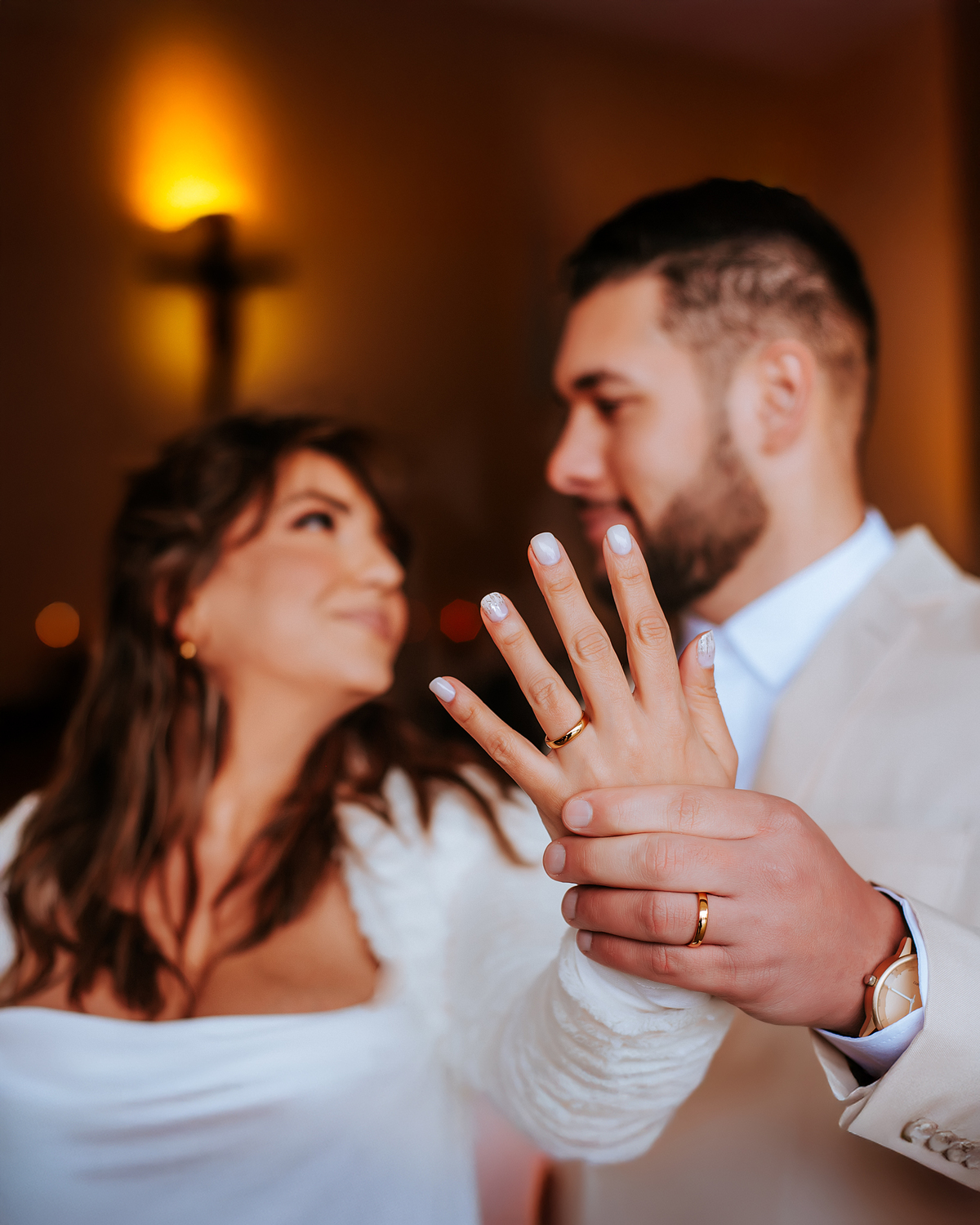 Noiva mostra sua aliança de casamento em primeiro plano enquanto troca olhares com o noivo durante a sessão fotográfica.