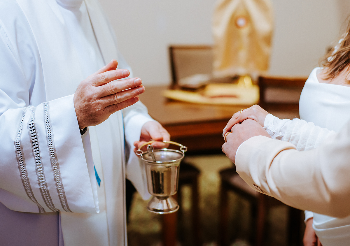 Detalhe das mãos durante um momento de bênção conduzido por um sacerdote na igreja, após o casamento civil.