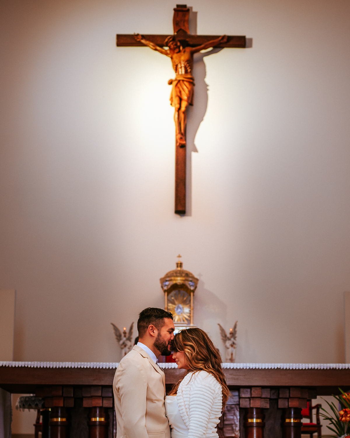 Fotografia do interior da igreja com crucifixo na parede e altar religioso, ambiente escolhido para os registros do casal.