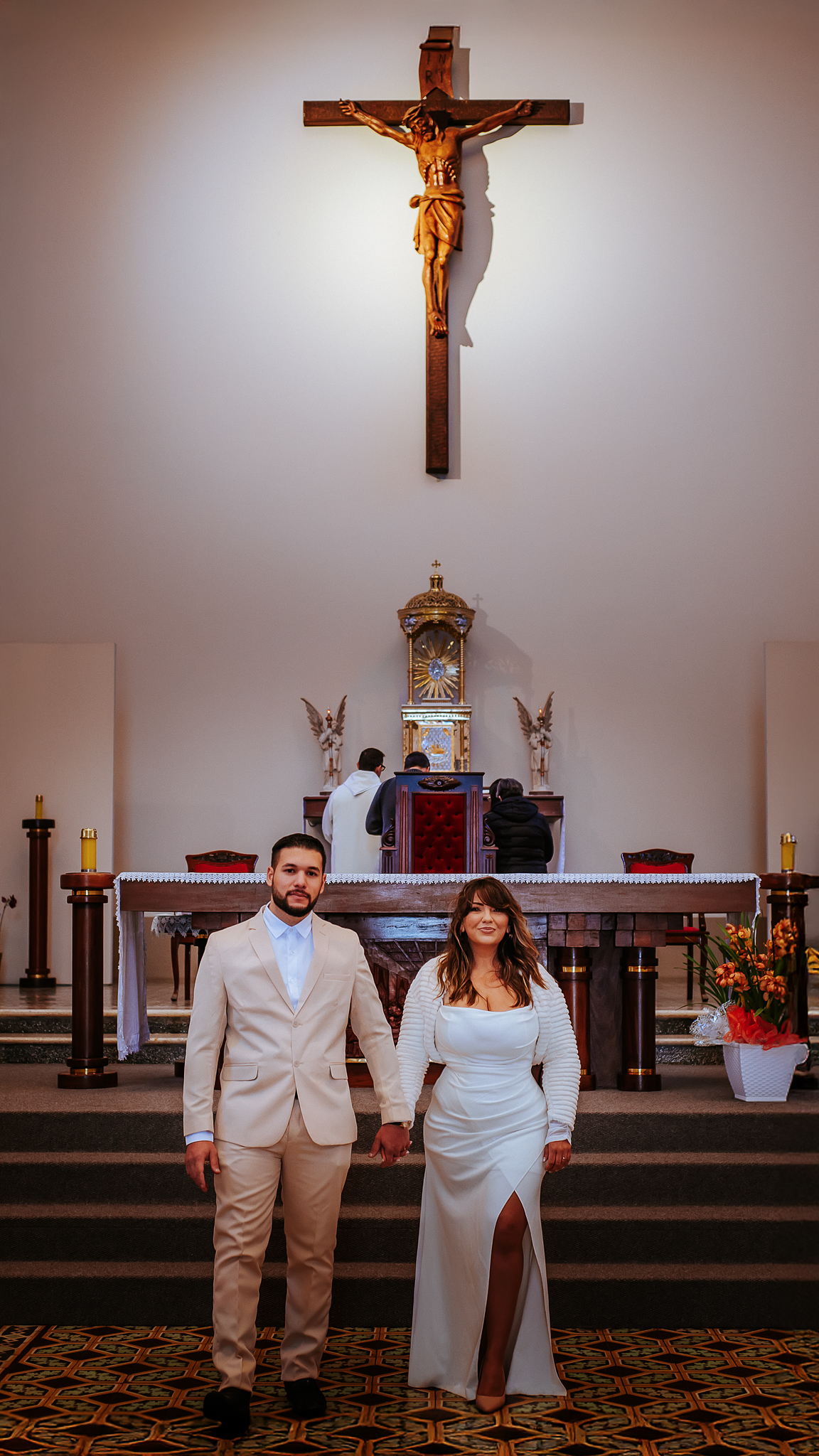 Noivos fotografados juntos diante do altar de uma igreja, com elementos religiosos ao fundo, após a celebração do casamento.