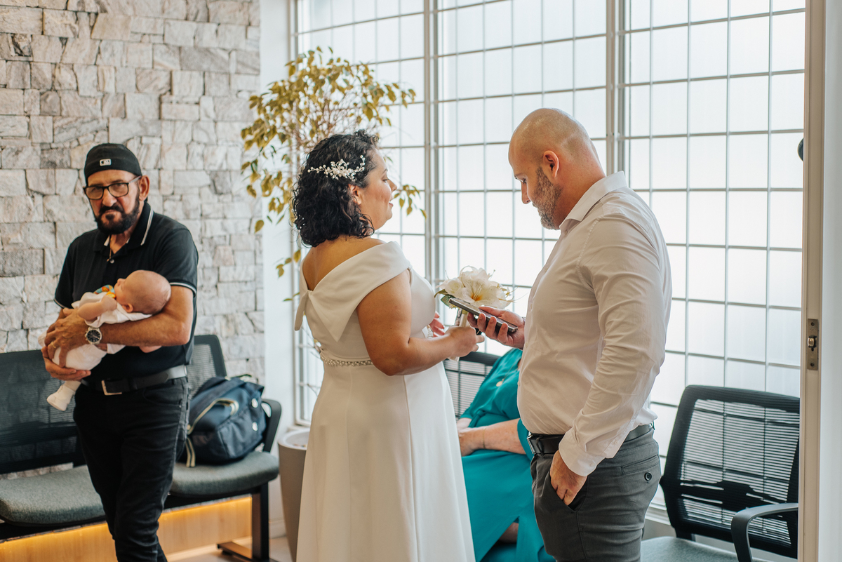 Stefhanie e John conversam durante o casamento civil, com o bebê do casal no colo de um convidado ao fundo.