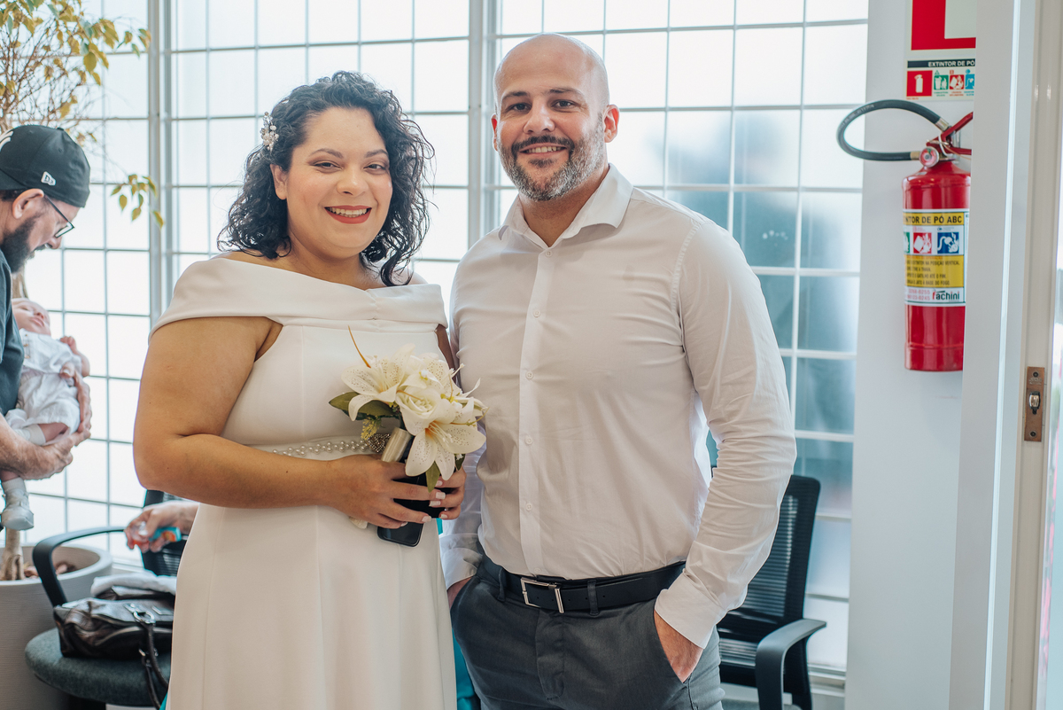 Stefhanie segura um buquê de flores brancas ao lado de John durante seu casamento civil em Farroupilha.