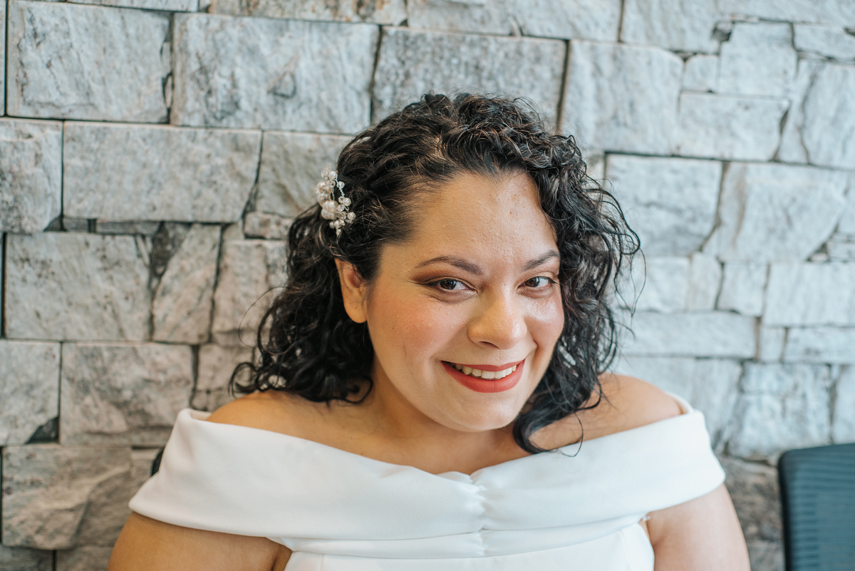 Retrato de Stefhanie sorrindo com vestido branco e cabelo cacheado durante seu casamento civil.