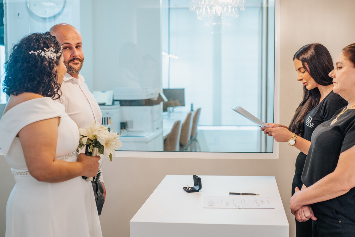 Stefhanie e John acompanham a fala de uma celebrante durante a cerimônia de casamento civil em Farroupilha.