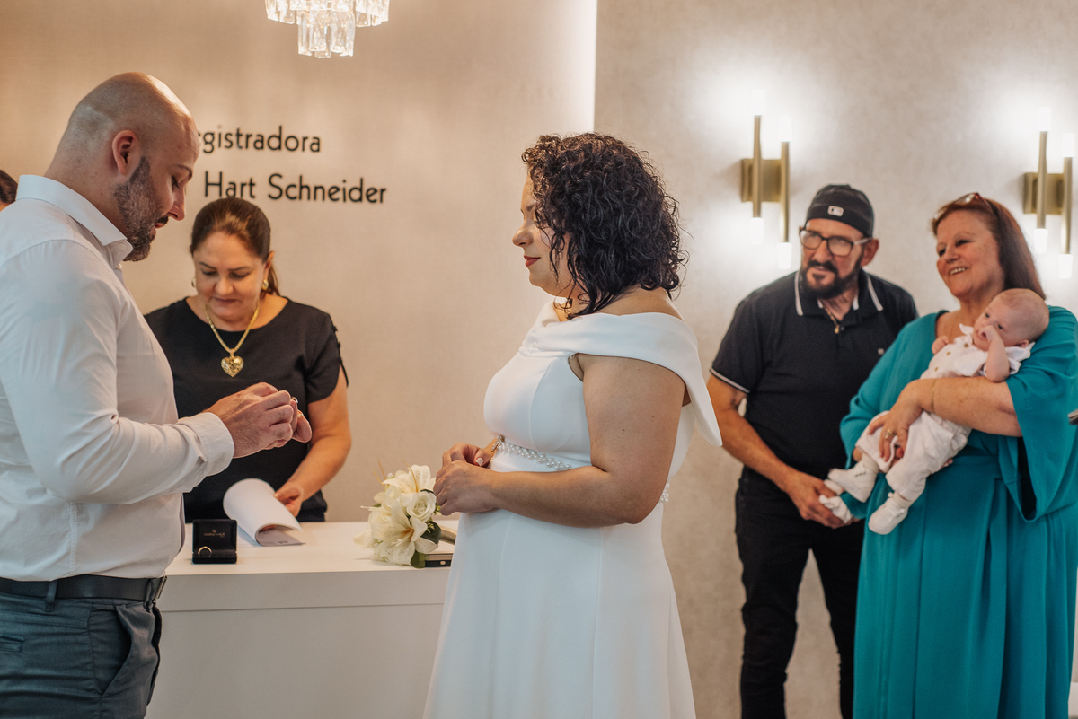 John e Stefhanie realizam a troca de alianças diante de familiares durante a cerimônia de casamento civil.