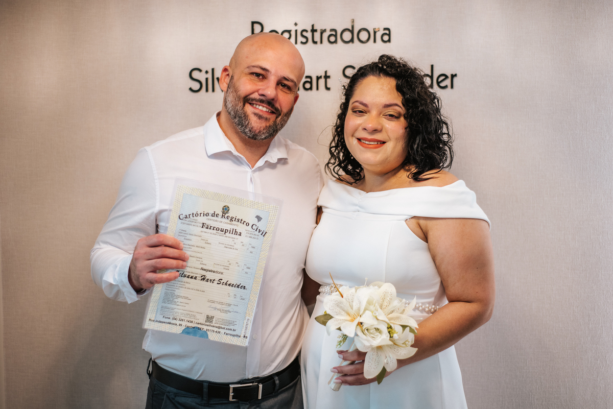 Stefhanie e John posam com o documento de casamento e um buquê branco após a cerimônia civil em Farroupilha.