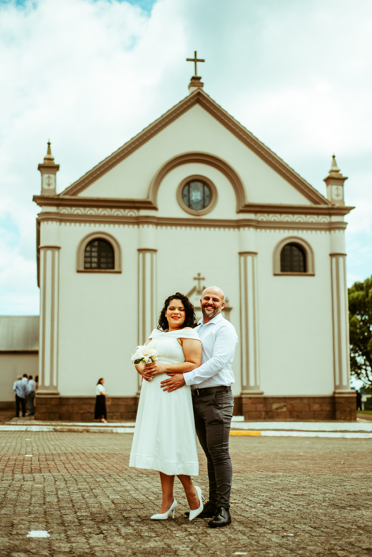 Fotografia de Stefhanie e John abraçados em frente ao Santuário de Caravaggio, na Serra Gaúcha.
