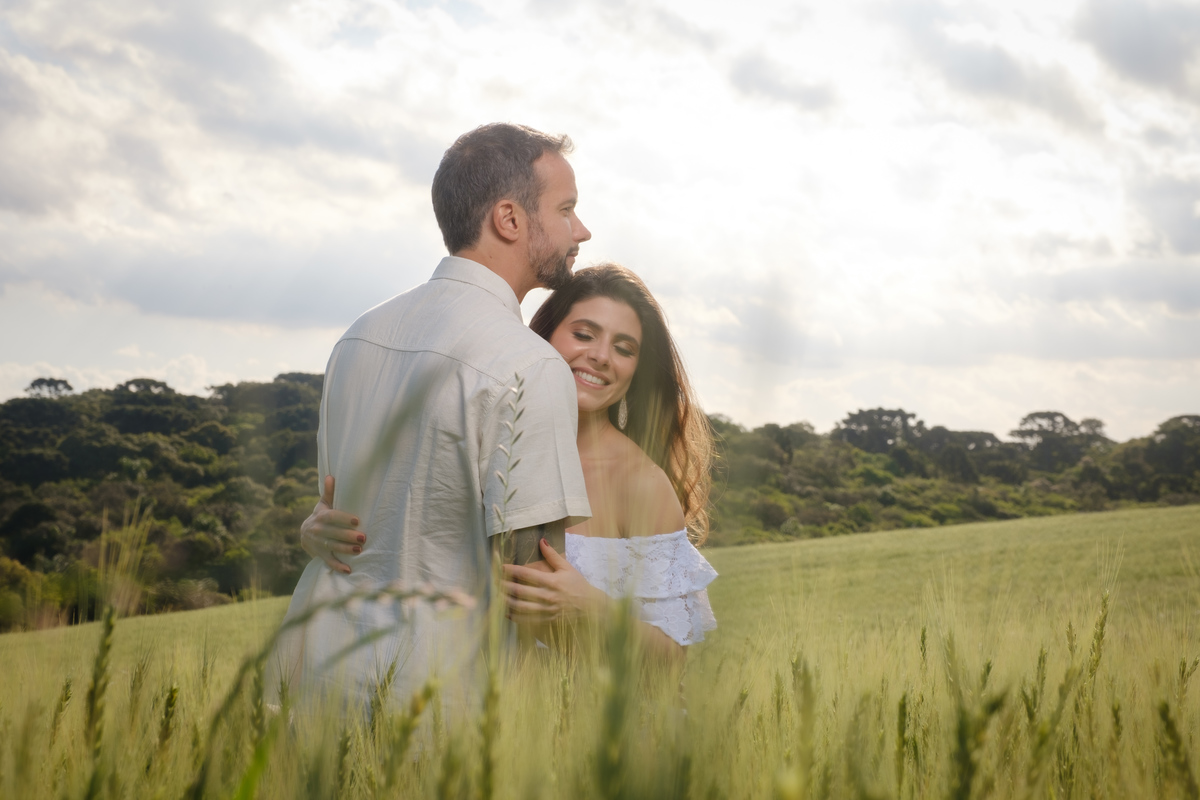 Ensaio de casal no Recanto Nogarotto em São José dos Pinhais com o noivo abraçando a noiva em fotografia ao ar livre em meio ao campo de trigo
