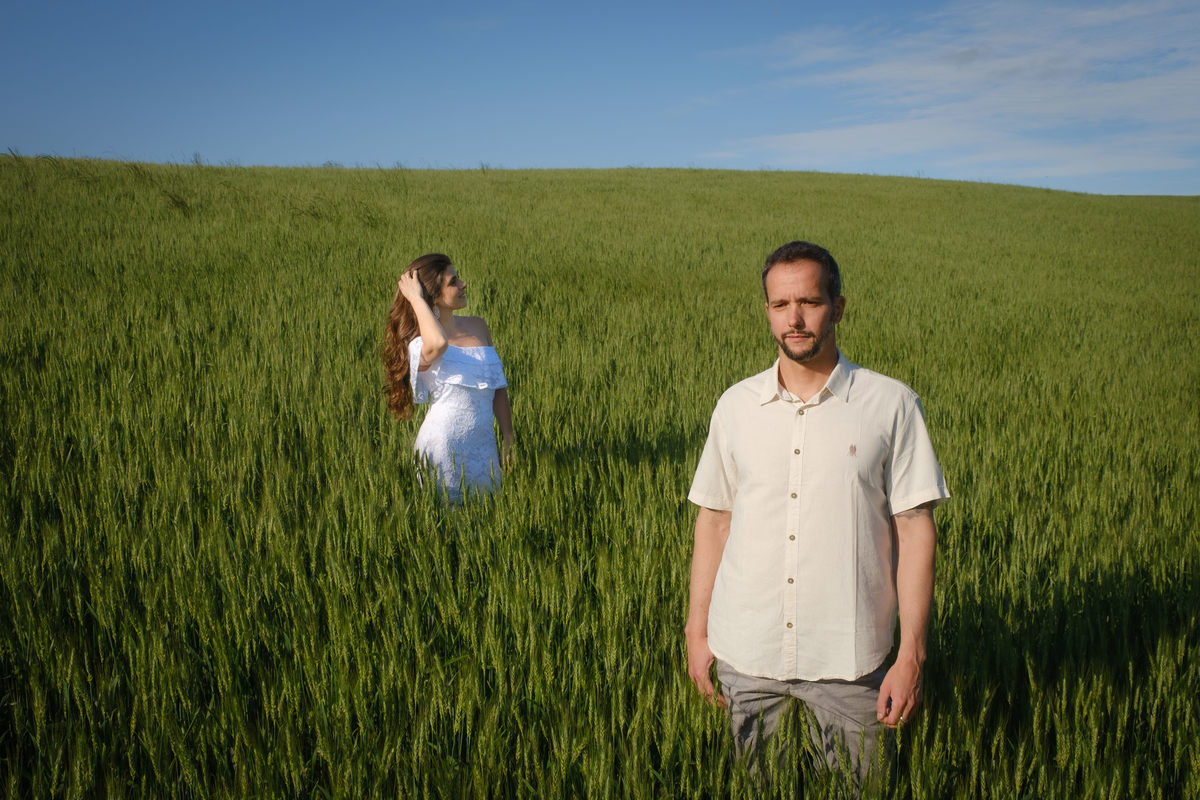 Fotografia de ensaio de casal em meio ao campo de trigo ao ar livre no Recanto Nogarotto em São José dos Pinhas com a noivo em primeiro plano e a noiva em segundo plano mexendo nos cabelos