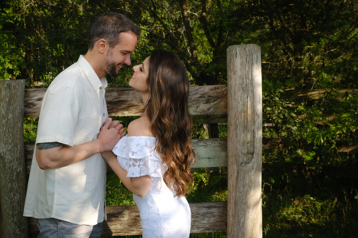 Noivo e noiva de frente um para o outro e de mãos dadas e sorrindo em frente a porteira de madeira no Recanto Nogarotto em São José dos Pinhais