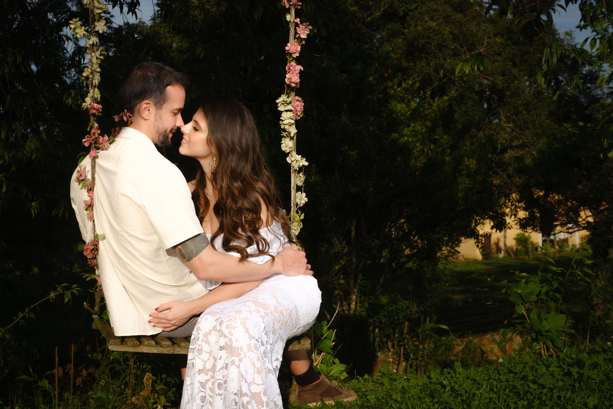 Noiva e noivo sentados em balanço com as cordas decoradas com flores em ensaio de casal no Recanto Nogarotto em São José dos Pinhais