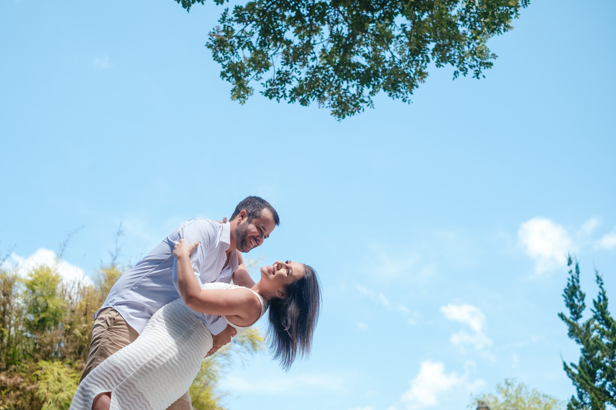 O noivo inclina o seu corpo e segura a noiva inclinando-a para trás. Ele olha para ela que olha para o lado e sorri