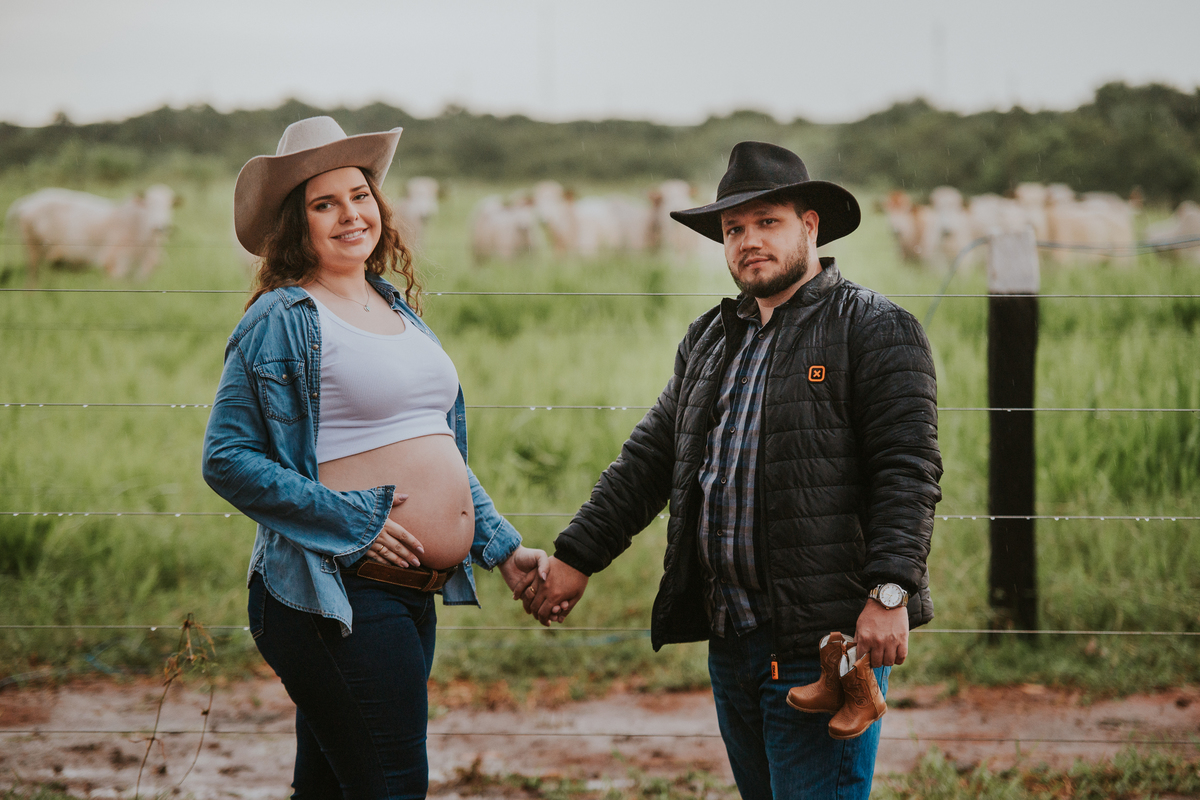 Gestante posando no curral com camisa jeans e chapéu country.