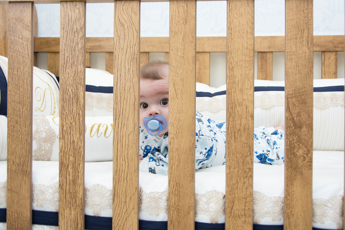 bebê de pijama chupando chupeta no berço