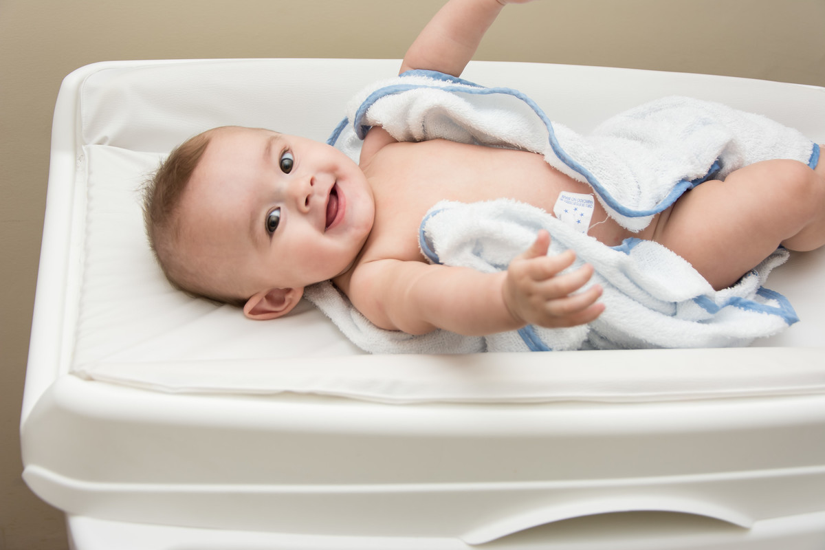 bebê sorrindo de toalha no trocador depois do banho
