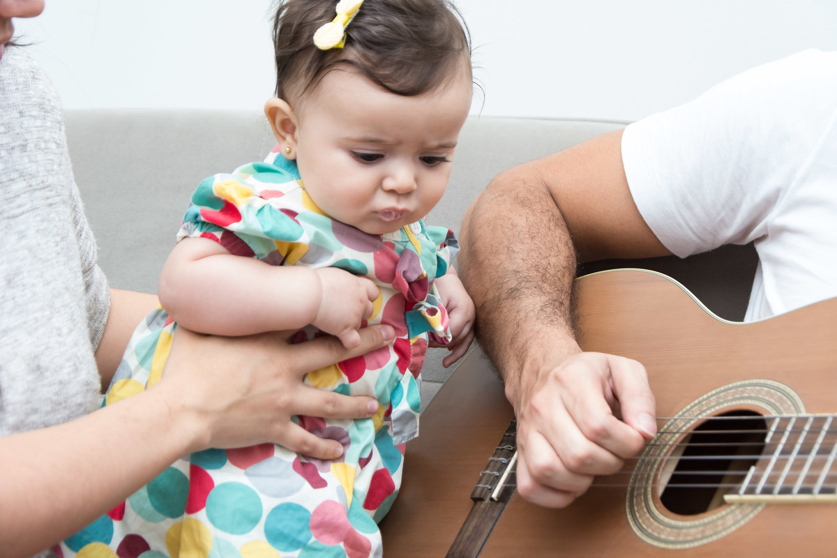 bebê com lacinho na cabeça olhando papai tocando violão