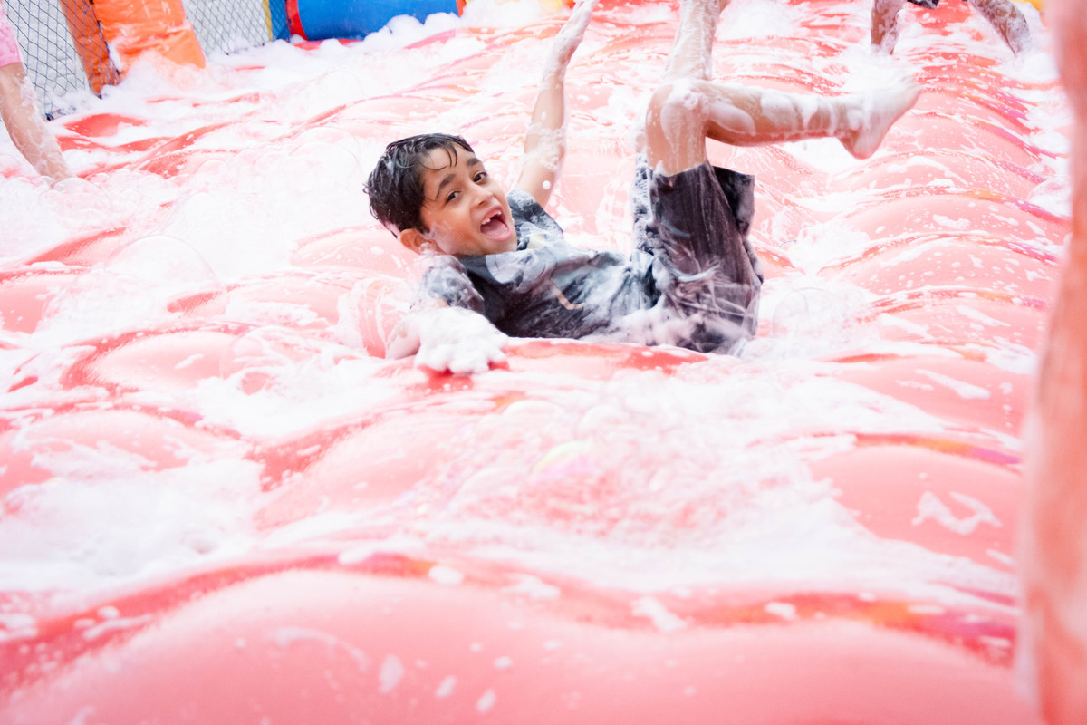Criança brincando na chuva jogando futebol de sabão