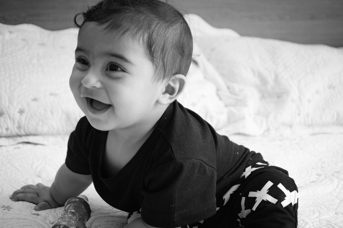 Bebê em cima da cama de perfil sorrindo por Paty Ramalho Fotografa de Itaquaquecetuba - SP