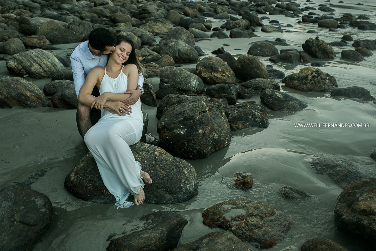 casal sentado sobre uma pedra na praia da baleia