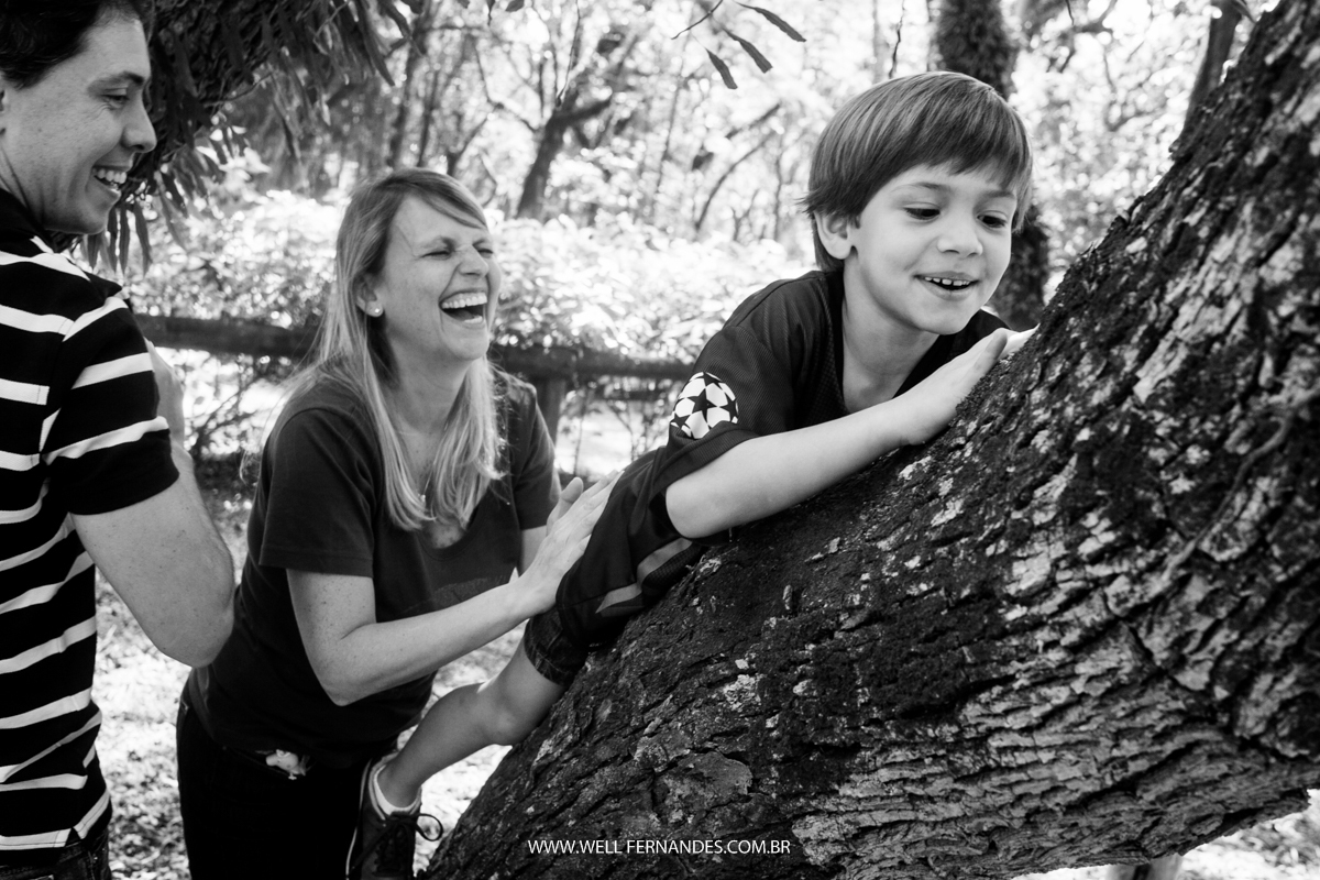 mãe e pai sorrindo enquanto seu filho sobe na arvore