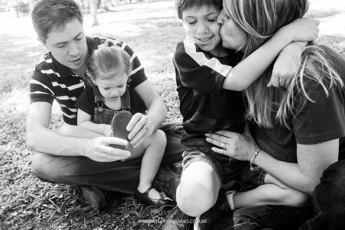 Mãe beijando o filho enquanto o pai arruma o chinelinho da irma