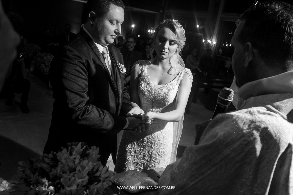 noivos segurando juntos a aliança e o padre aebnçoando