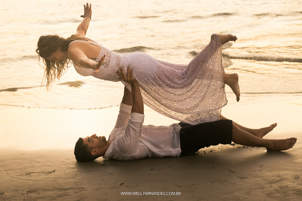 noivo levantando a noiva em seus braços deitados na areia do mar