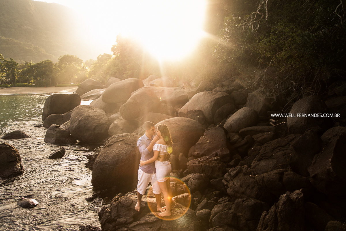 raios de luz iluminando o casal no ensaio pre wedding em cima das pedras em ubatuba