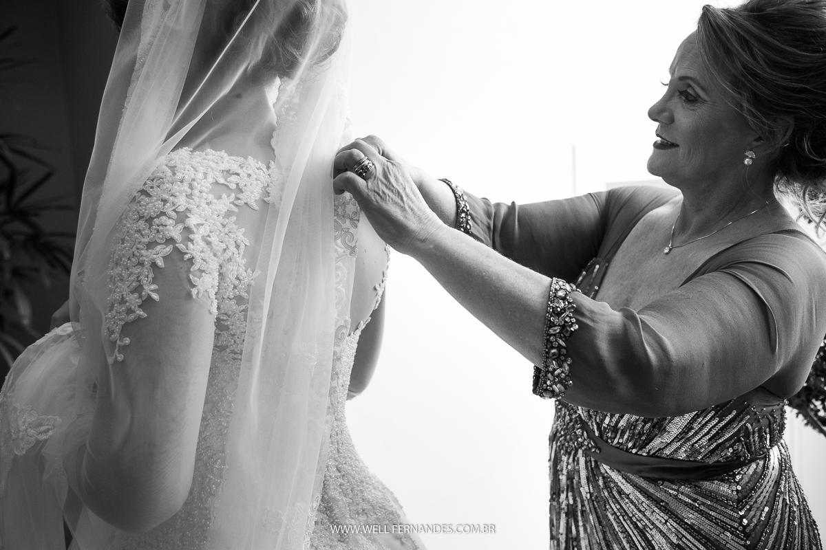 mae sorridente ajudando a noiva a colocar o vestido
