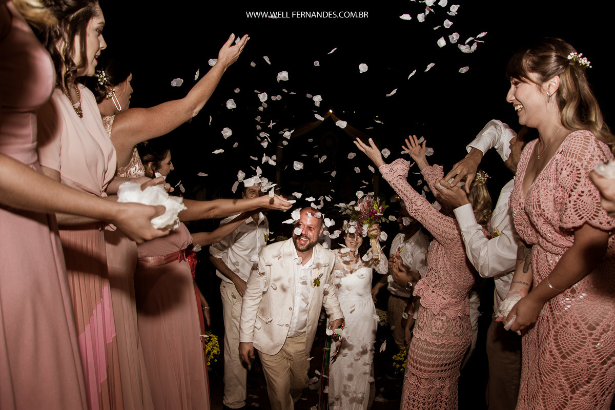 noivos saindo e padrinhos jogando petalas para o alto
