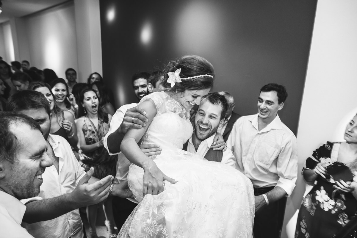 Noivo Pedro pegando no colo a noiva Karine na festa de casamento na Galeria Scenarium/Rio Scenarium, Rio de Janeiro/RJ