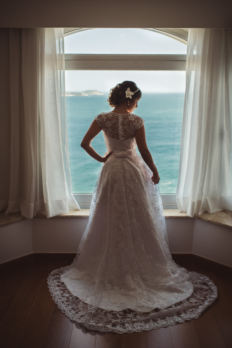 Noiva Karine olhando seu vestido com vista para a praia de Ipanema no making of no Caesar Park Ipanema, Rio de Janeiro/RJ