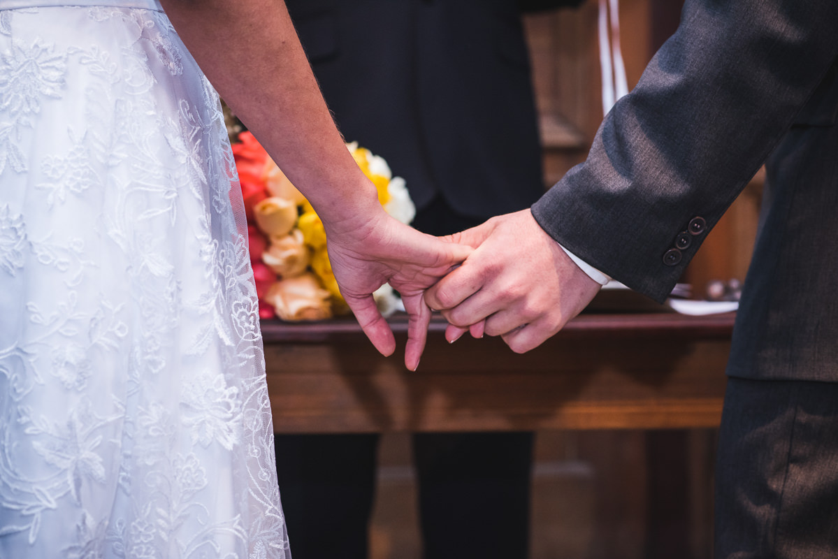 Mãos unidas dos noivos Karine e Pedro na celebração do casamento na Galeria Scenarium/Rio Scenarium, Rio de Janeiro/RJ