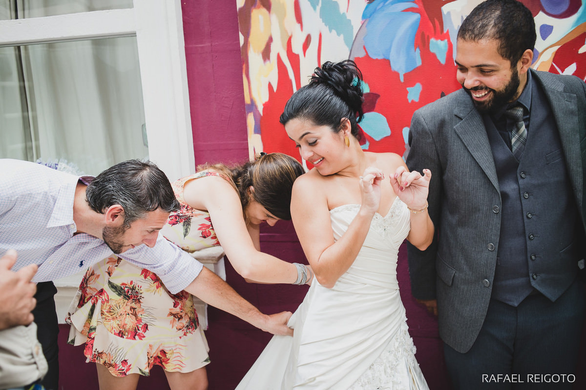 Amigos e amigas ajudando a noiva com seu vestido após a celebração do casamento budista do casal Beatriz e Roger no Drink Café Humaitá, Humaitá, Rio de Janeiro-RJ
