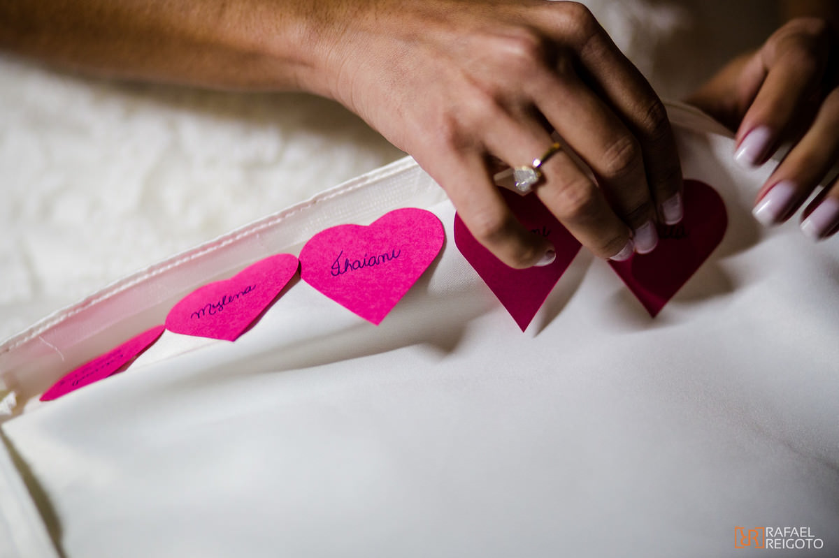 Noiva Talita colando os corações com o nome das amigas solteiras na barra do vestido no seu making of em São Conrado, Rio de Janeiro/RJ