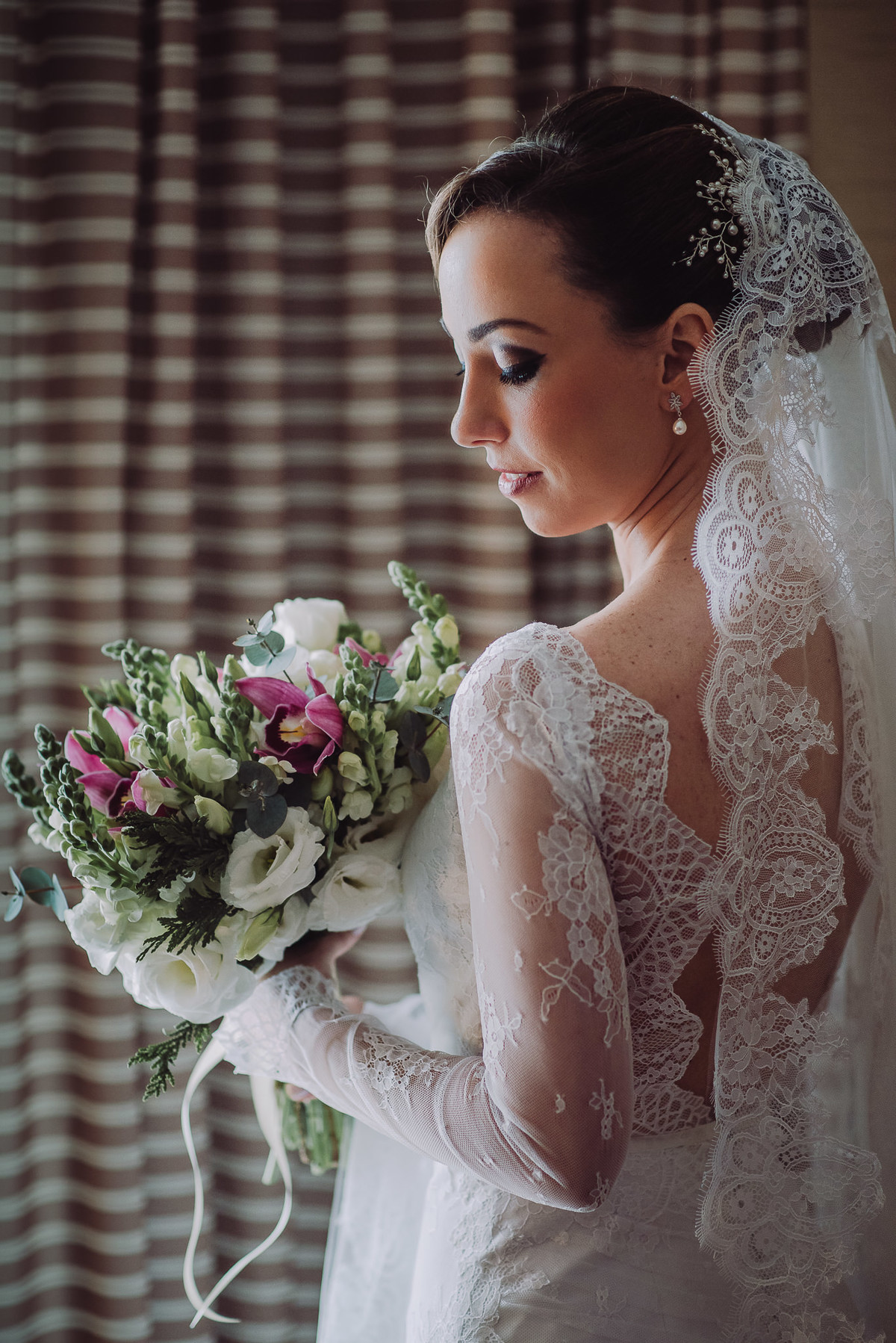A noiva Luana olhando para o seu buquê de rosas e orquídeas no seu making of no Hotel Sheraton, Leblon, Rio de Janeiro-RJ