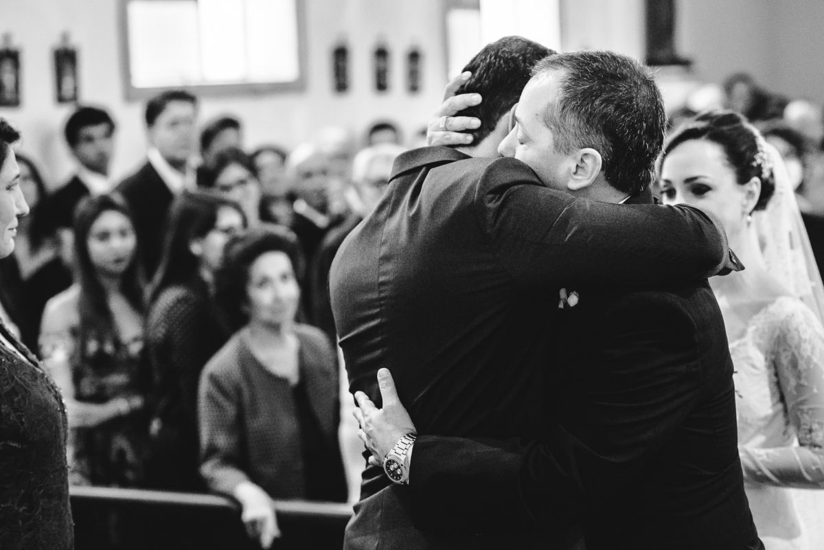 O noivo Julio abraçando emocionado o pai de sua  noiva no momento que ele chega com sua filha Luana ao altar da Capela Santa Ignez, Gávea, Rio de Janeiro-RJ