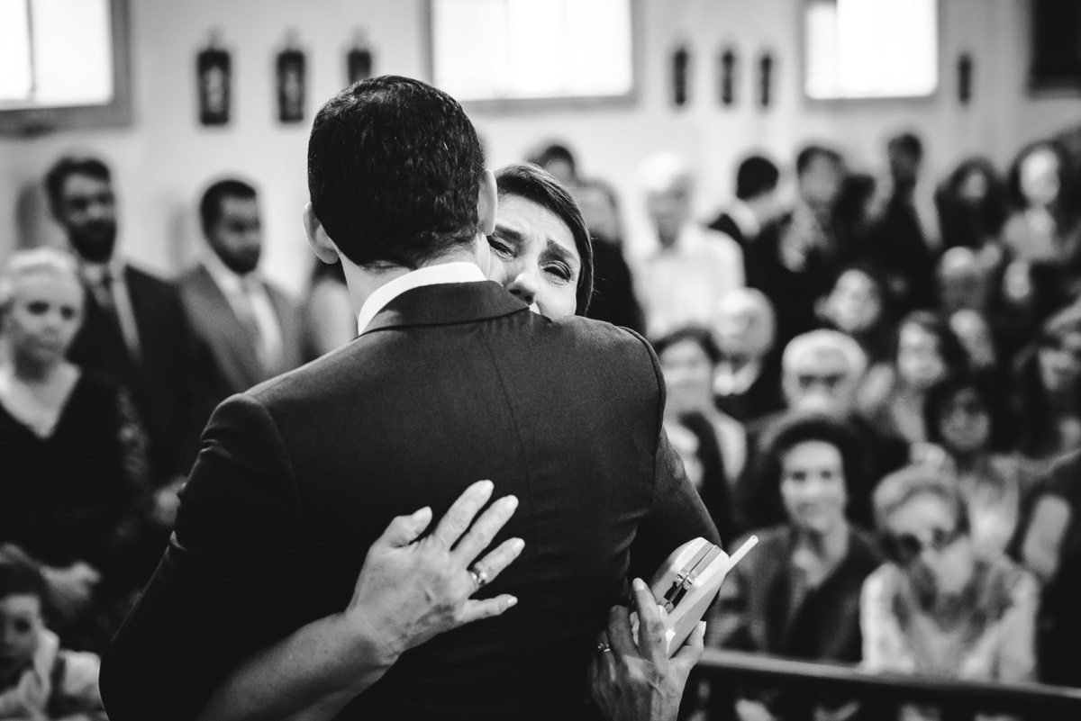 A mãe do noivo Julio abraçando emocionada o seu filho após a celebração do casamento na Capela Santa Ignez, Gávea, Rio de Janeiro-RJ
