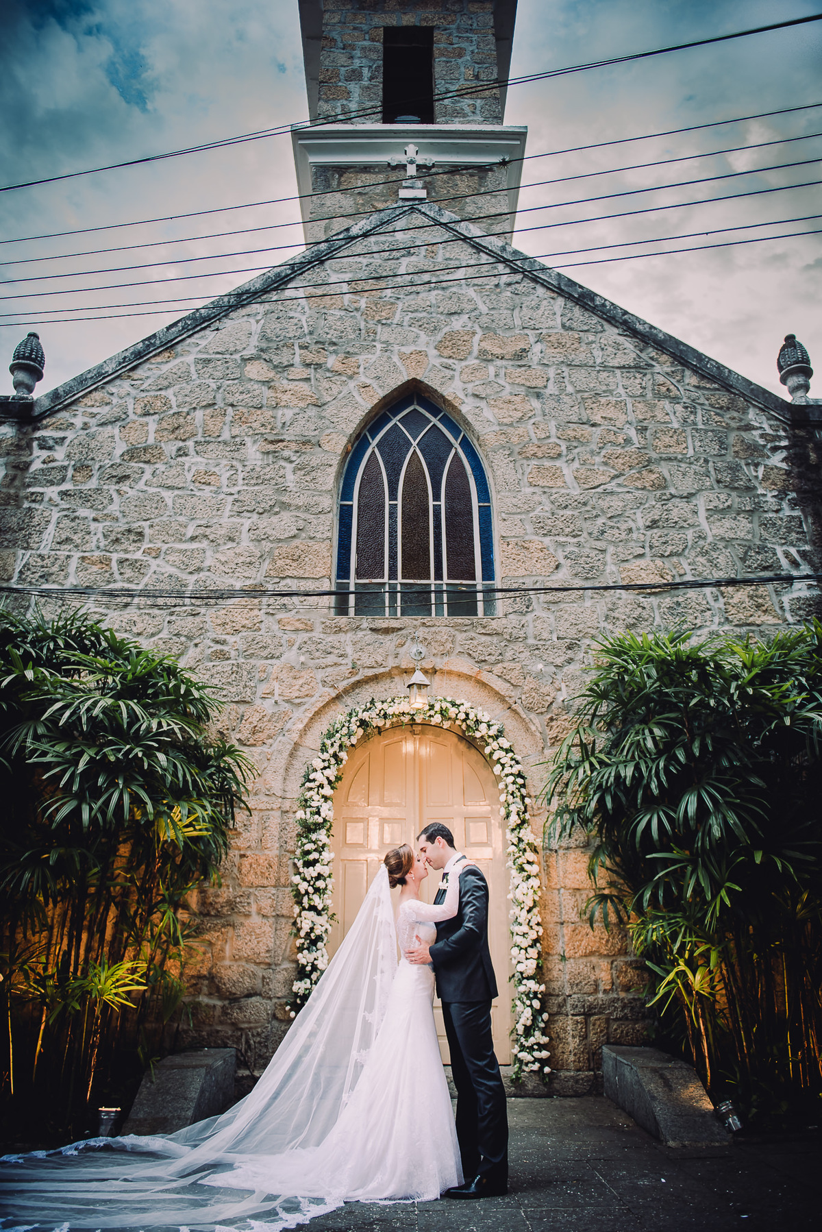O casal Luana e Julio em linda foto em frente a Capela Santa Ignez no ensaio após a celebração do casamento, Gávea, Rio de Janeiro-RJ.