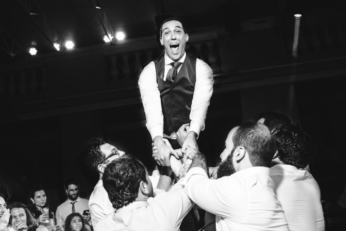 Padrinhos e convidados jogando o noivo Julio para o alto na pista de dança do seu casamento no salão da Capela Santa Ignez, Gávea, Rio de Janeiro-RJ.