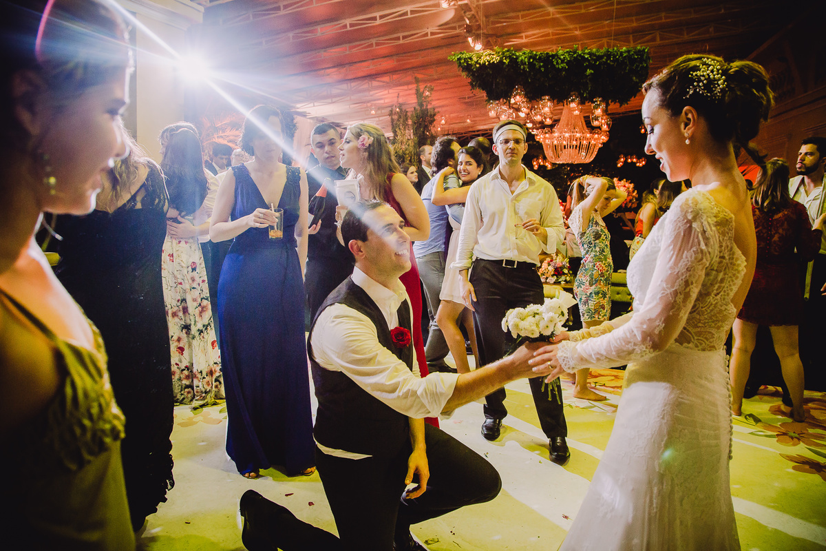 Noivo Júlio ajoelhado no meio da pista de dança entregando um buquê de flores para a noiva Luana na festa de seu casamento no  salão da Capela Santa Ignez, Gávea, Rio de Janeiro-RJ.
