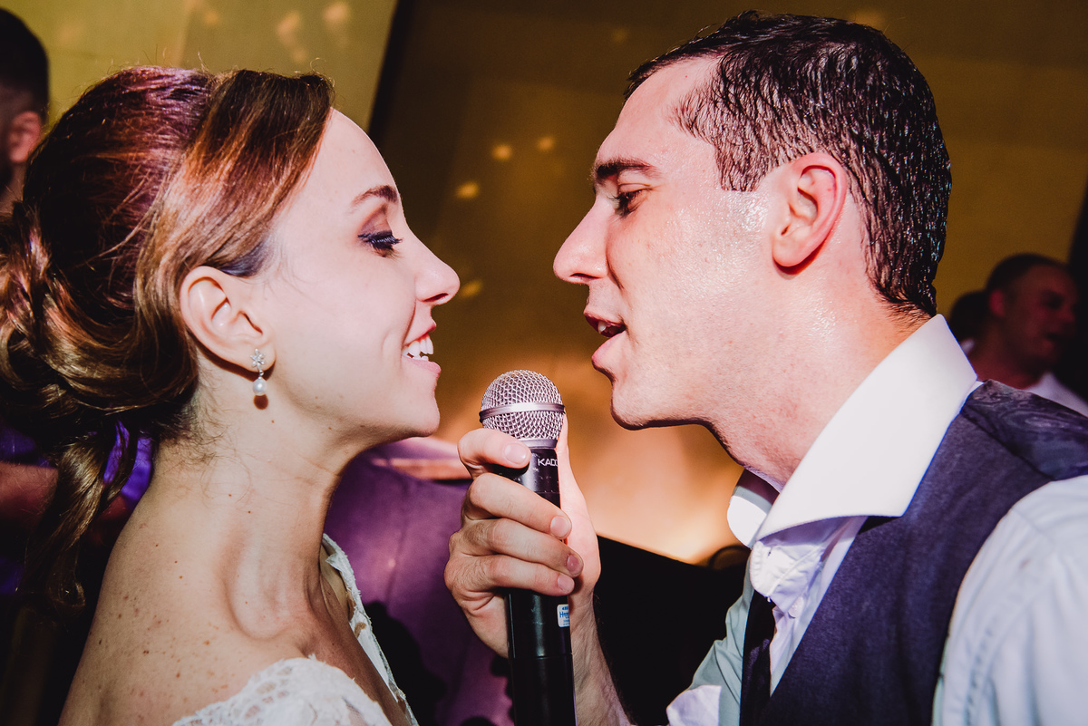 Noivos Luana e Julio cantando no microfone da banda no seu casamento no salão da Capela Santa Ignez, Gávea, Rio de Janeiro-RJ.