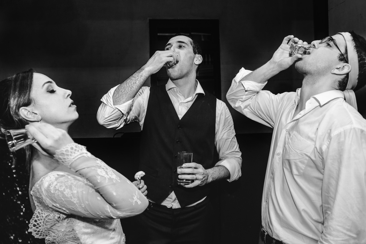 Noivo Júlio e seu amigo bebendo um shot, enquanto a noiva Luana disfarçava e jogava para trás a bebida na festa de seu casamento no  salão da Capela Santa Ignez, Gávea, Rio de Janeiro-RJ.