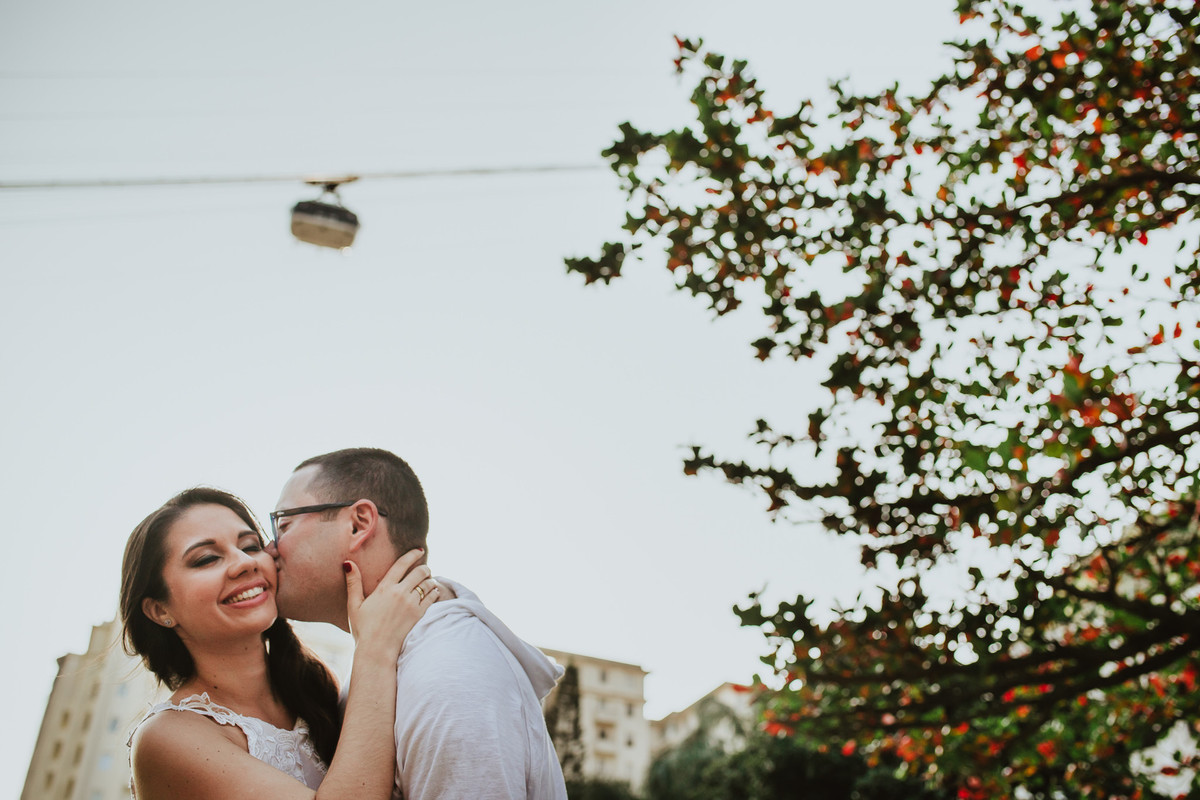 O noivo Raphael dando um beijo em sua noiva Bruna com o bondinho do Pão de Açúcar passando ao fundo, Urca, Rio de Janeiro/RJ