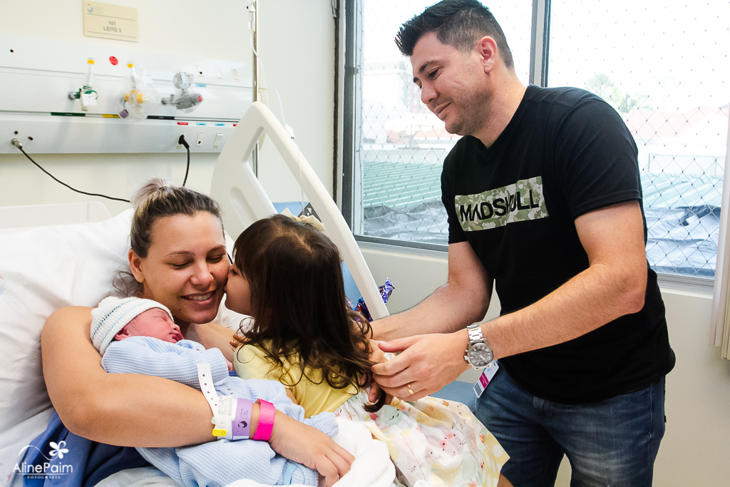mamãe Daniele recendo carinho da filha mais velha de 3 anos, e segurando seu bebezinho theo, fotografia feita pela fotografa aline paim fotografia