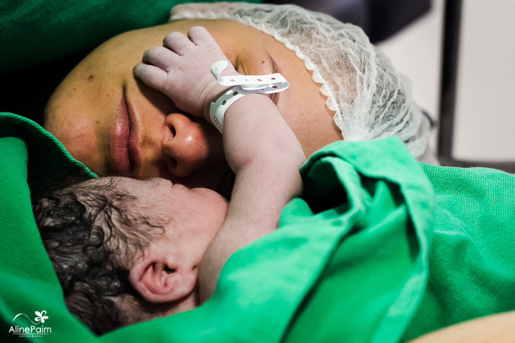 na fotografia do parto fotografada por aline paim, o bebezinho estava chorando, quando sentiu o cheiro da mamãe, logo deixou sua mãozinha em cima do rosto da mamãe