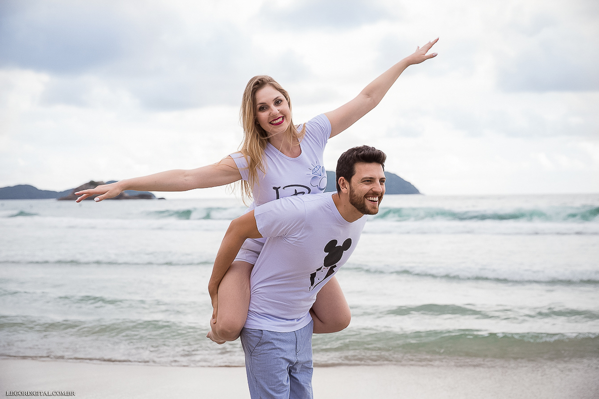 noiva nas costas do noivo com camiseta do mickey e minnie na praia de Juquehy no pré-wedding em Guarujá-SP