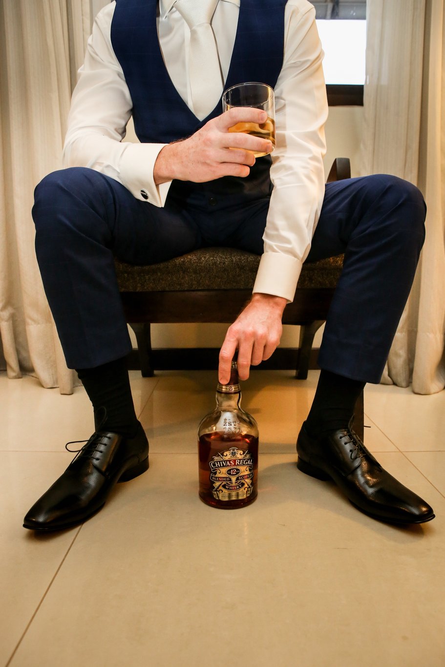 noivo com um copo de wisk na mao e a outra mao no vidro de wisk e ja com seu terno foto tirada pelo fotografo de casamento thiago alt