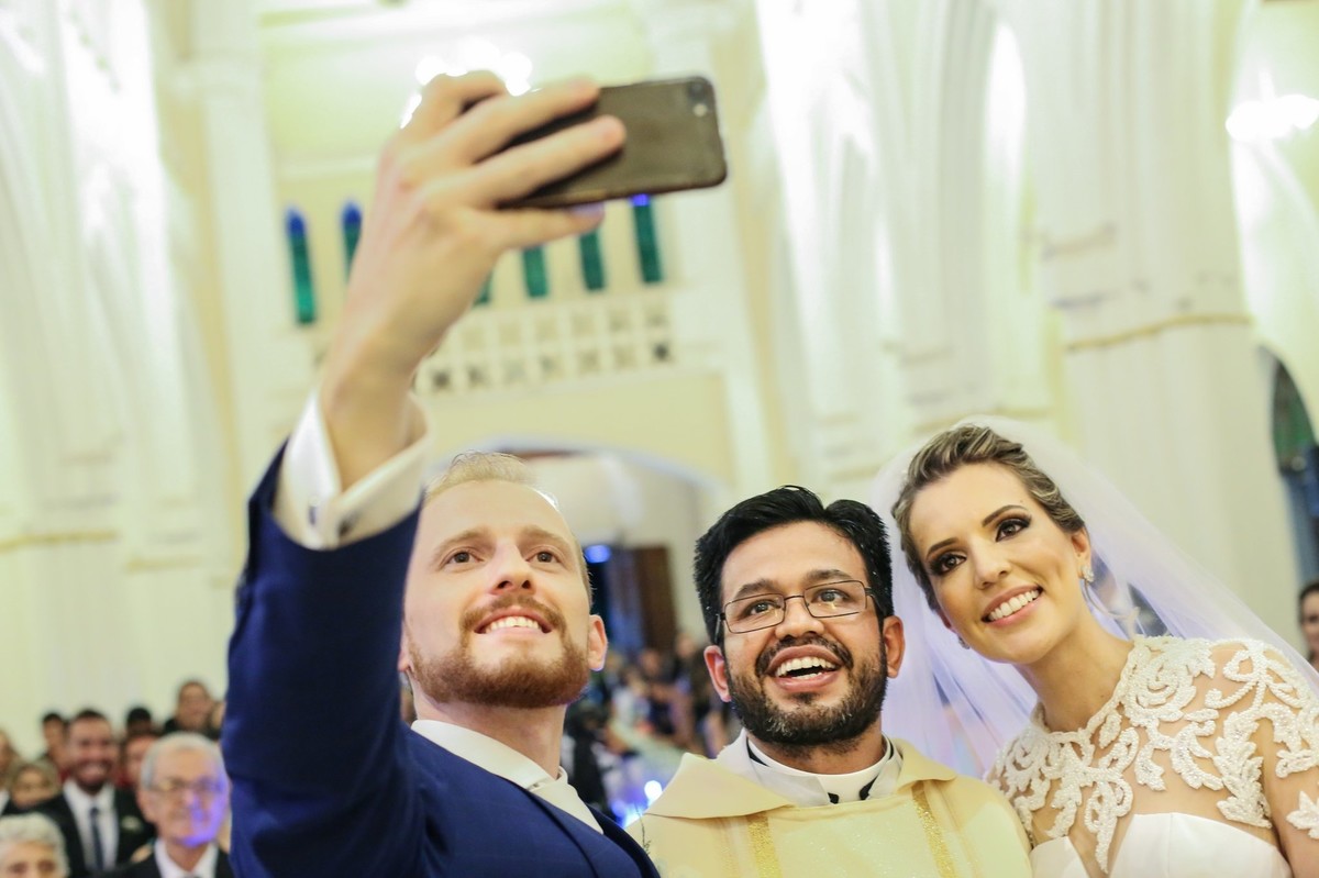 noivo com seu iphone tirando foto com padre e com sua noiva na igrej ado bom despacho  foto tirada nas lentes do fotografo thiago alt